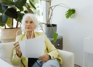 Senior woman sitting on a couch, reviewing a document with a thoughtful expression, symbolizing the process of applying for senior assistance programs.