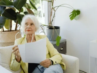 Senior woman sitting on a couch, reviewing a document with a thoughtful expression, symbolizing the process of applying for senior assistance programs.