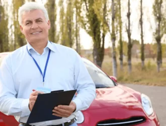 Senior driving instructor with clipboard, standing by a red car, illustrating new drivers license rules for seniors