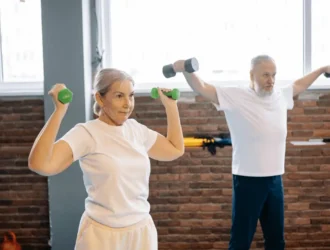 Senior man and woman doing dumbbell exercises together in a gym, focusing on strength training for seniors.