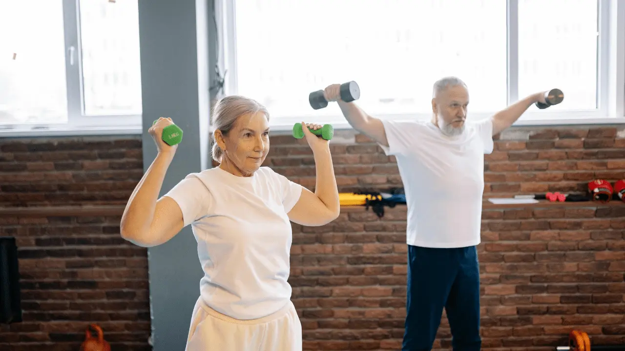 Senior man and woman doing dumbbell exercises together in a gym, focusing on strength training for seniors.