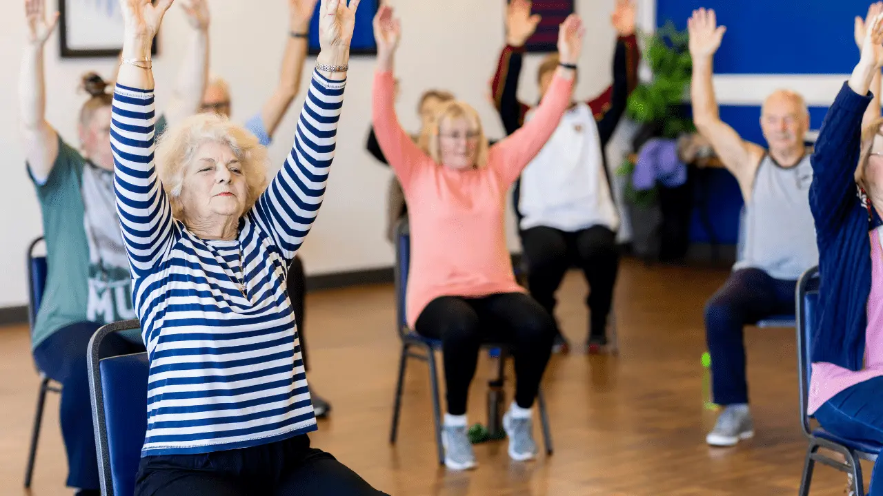 Seniors participating in a seated workout class, lifting their arms in a fitness session.