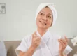 Senior woman applying perfume, enjoying a moment of self-care in a cozy, relaxed setting.