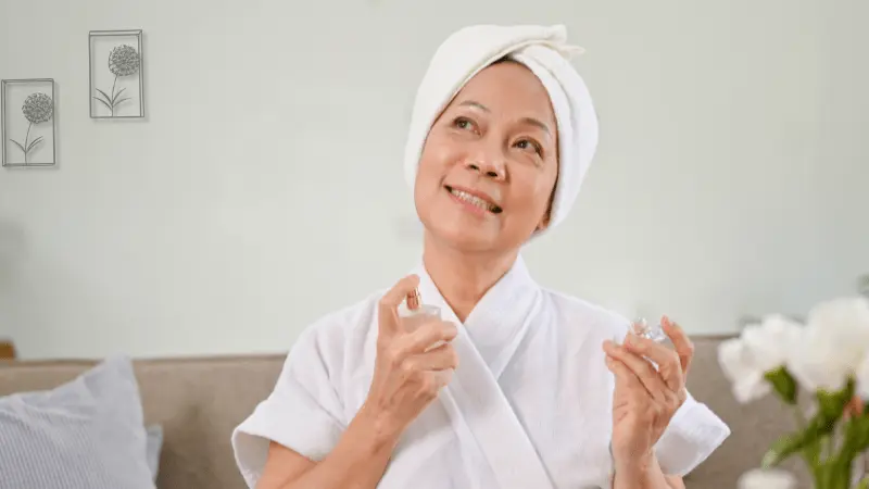 Senior woman applying perfume, enjoying a moment of self-care in a cozy, relaxed setting.