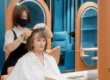 A senior woman receiving a stylish haircut in a modern salon, showcasing a low-maintenance hairstyle suitable for thin hair. A hairdresser is trimming her hair, helping her achieve a fuller, youthful look with minimal effort
