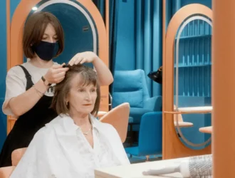 A senior woman receiving a stylish haircut in a modern salon, showcasing a low-maintenance hairstyle suitable for thin hair. A hairdresser is trimming her hair, helping her achieve a fuller, youthful look with minimal effort