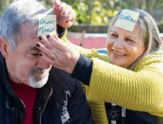 Elderly couple playing a fun word game together with sticky notes on their foreheads, engaging in a memory-boosting and social activity.