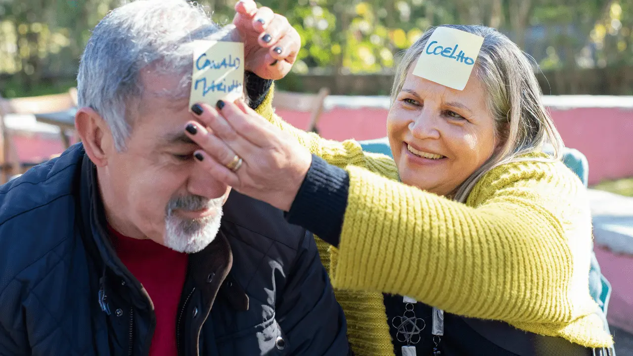 Elderly couple playing a fun word game together with sticky notes on their foreheads, engaging in a memory-boosting and social activity.