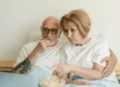 Senior couple watching a movie together at home with popcorn, enjoying streaming services.