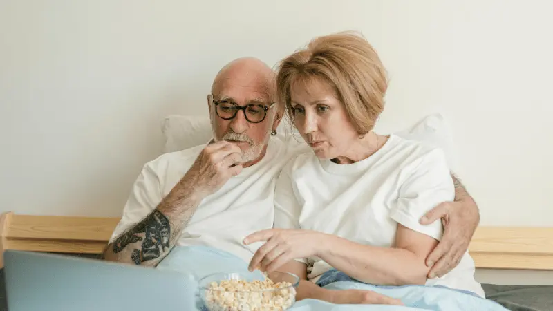 Senior couple watching a movie together at home with popcorn, enjoying streaming services.