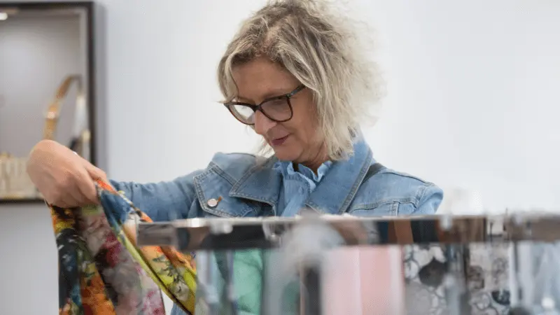 Senior woman shopping for clothes, looking at colorful garments in a clothing store, enjoying a shopping experience with discounts for seniors