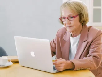 A senior woman working on a laptop, sitting at a table with a cup of coffee beside her. She is focused on her task, embodying the empowerment of seniors navigating Medicare and healthcare options independently. The image represents the engagement and decision-making process for seniors researching the best Medicare plans.