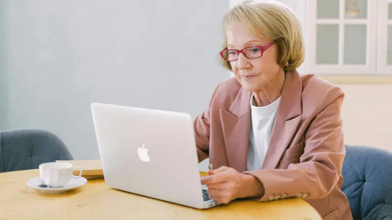 A senior woman working on a laptop, sitting at a table with a cup of coffee beside her. She is focused on her task, embodying the empowerment of seniors navigating Medicare and healthcare options independently. The image represents the engagement and decision-making process for seniors researching the best Medicare plans.
